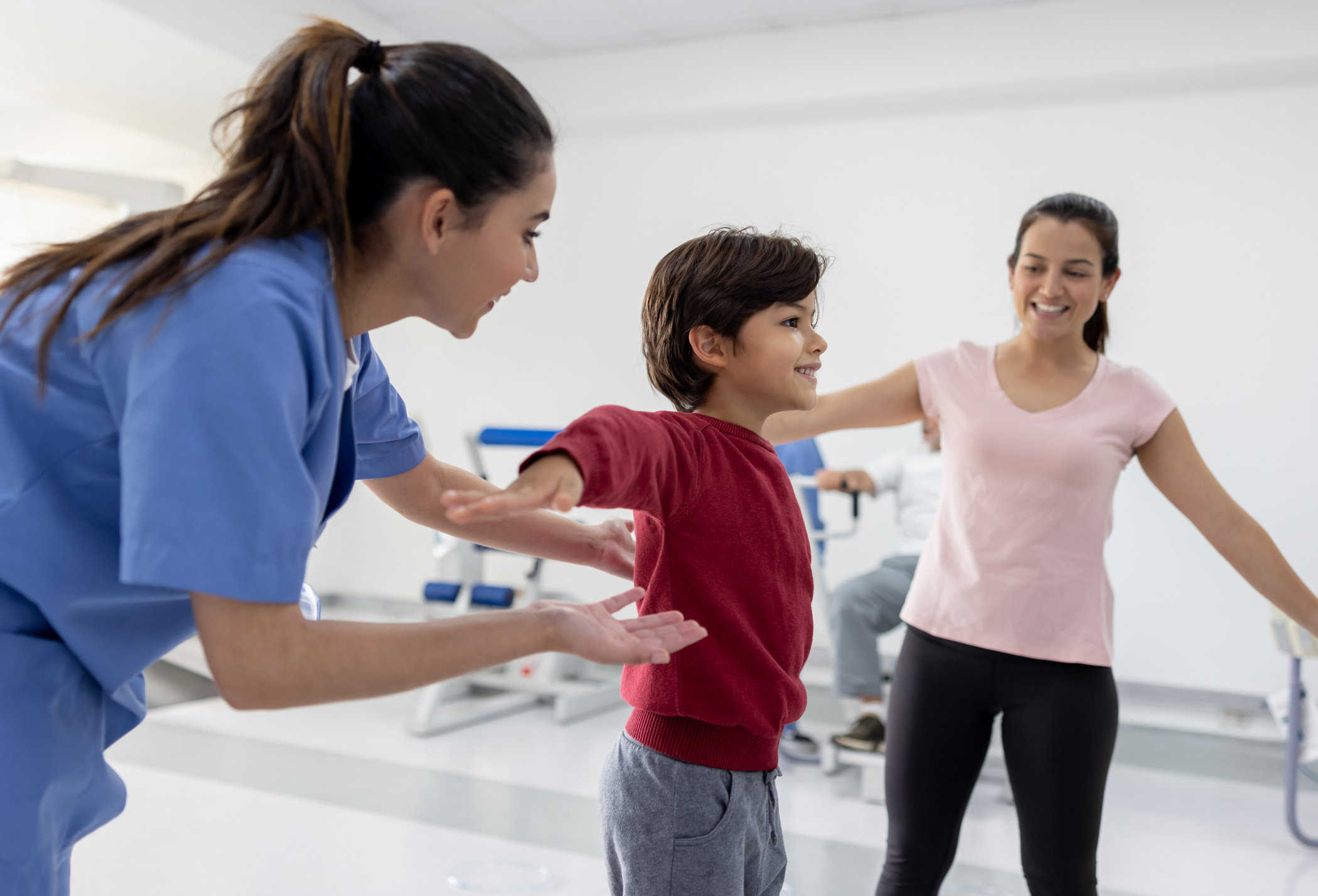 boy working on his balance in physical therapy with the help of his therapist and his mother for Happy Latin American boy working on his balance in physical therapy with the help of his therapist and his mother